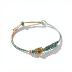 Handmade green cotton woven bracelet dyed with natural plant elements, featuring a central green tourmaline stone in a vintage gold setting woven with gold silk threads, Eastern Zen meditation jewelry.